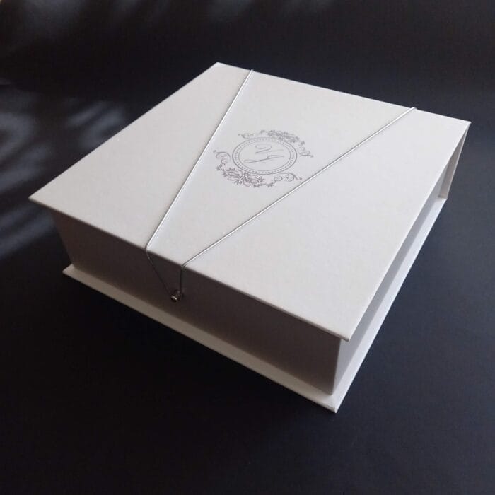 Caixa cartonada para padrinhos retangular, no tamanho 19x23 - Fechada com elástico cinza e brasão em prata artinvitte